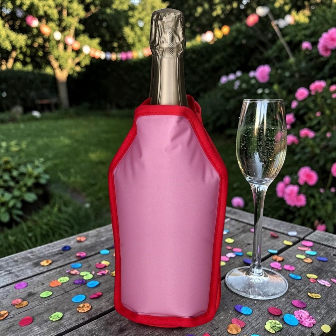 Nomafu Froid Kühlmanschette in Pink mit rotem Rand um eine Sektflasche auf einem Gartentisch mit Konfetti
