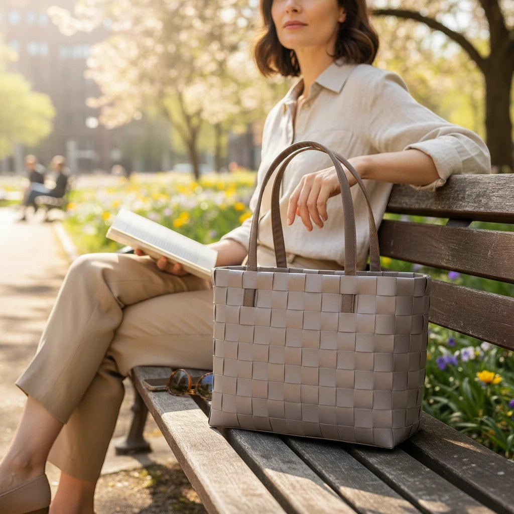 Nomafu ICE-BAG Chic Shopper in Taupe aus geflochtenem Recycling-Kunststoff mit Kunstlederhenkeln auf einer Parkbank.