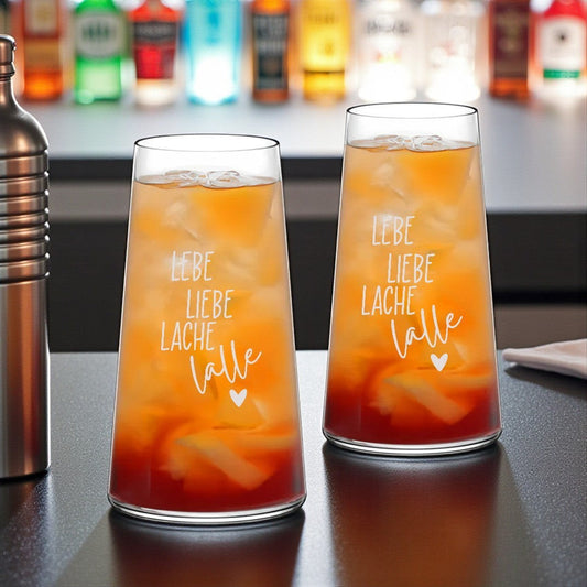Nomafu long drink glasses with Lebe Liebe Lache engraving filled with orange cocktails on a bar counter