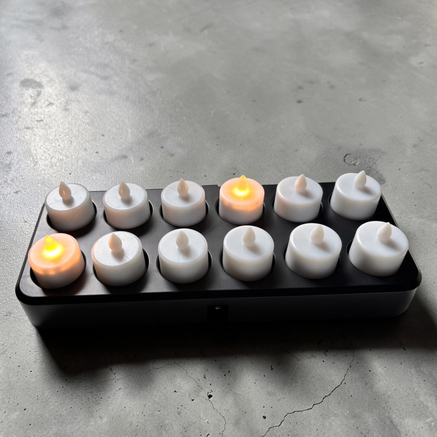 Nomafu set of 12 rechargeable LED tea lights with an inductive charging station, two lights glowing warm amber.