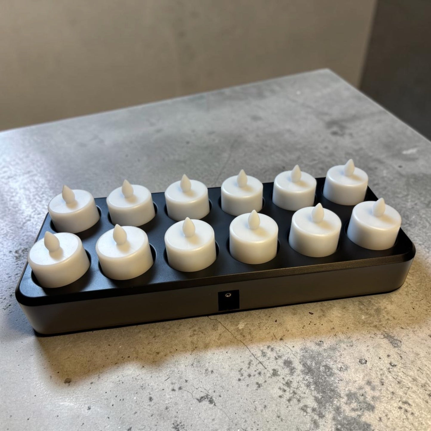 Nomafu set of 12 rechargeable LED tea lights with a black inductive charging station on a grey stone surface.