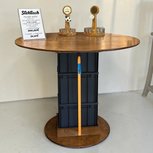 Nomafu Runde Kiste XXL round standing table with walnut-stained multiplex top, black beverage crates, and orange strap.