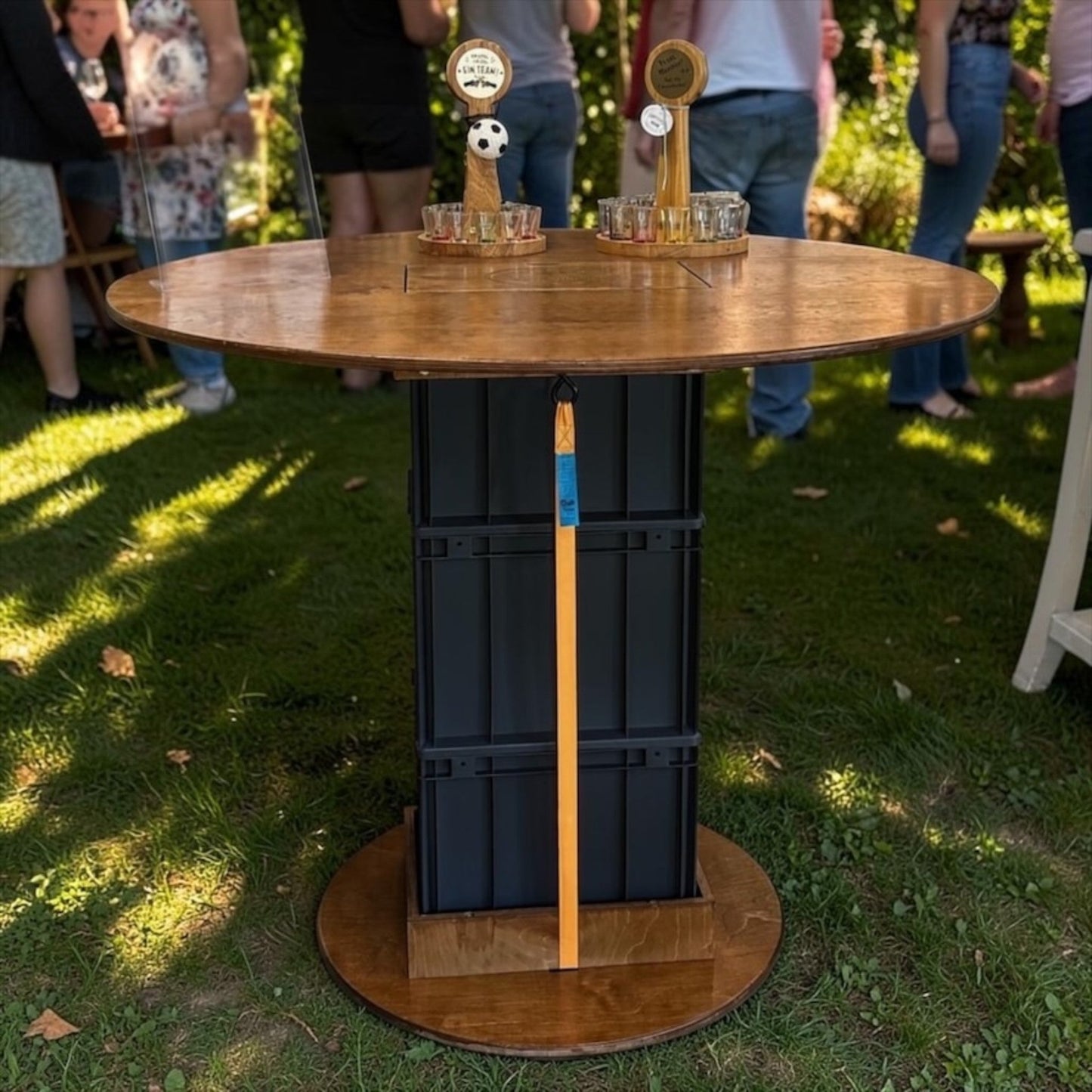 Nomafu Runde Kiste XXL standing table with walnut-stained wooden top and black beverage crate base on a lawn.