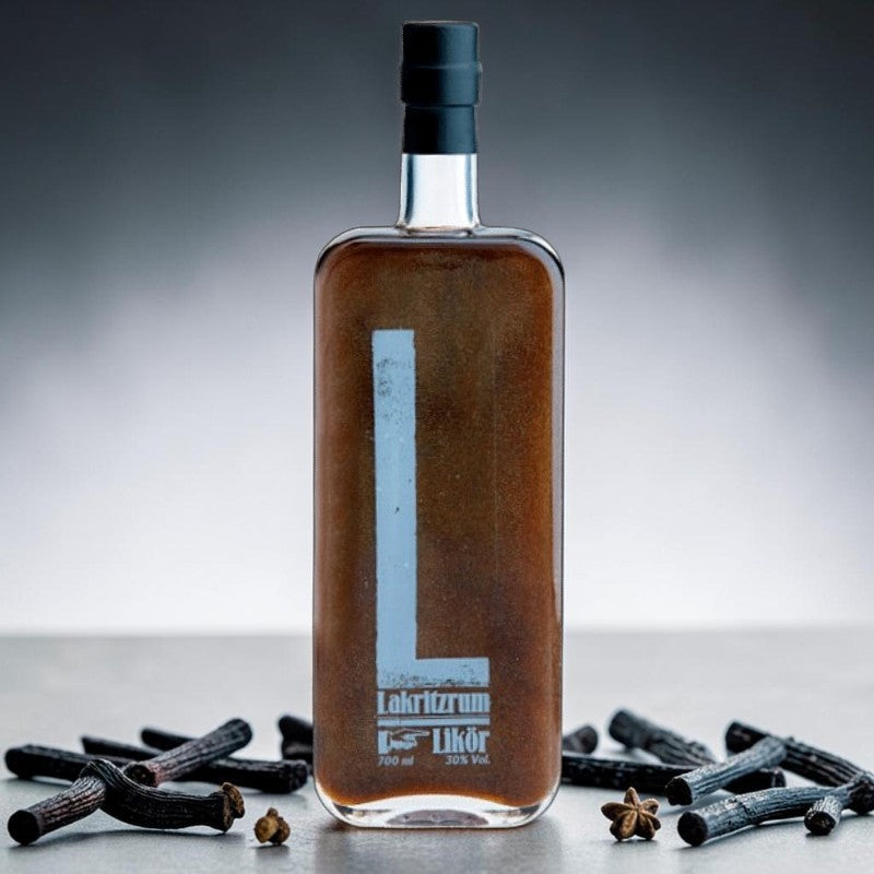 Nomafu Taste Deluxe liquorice rum liqueur in a tall glass bottle surrounded by liquorice sticks and star anise