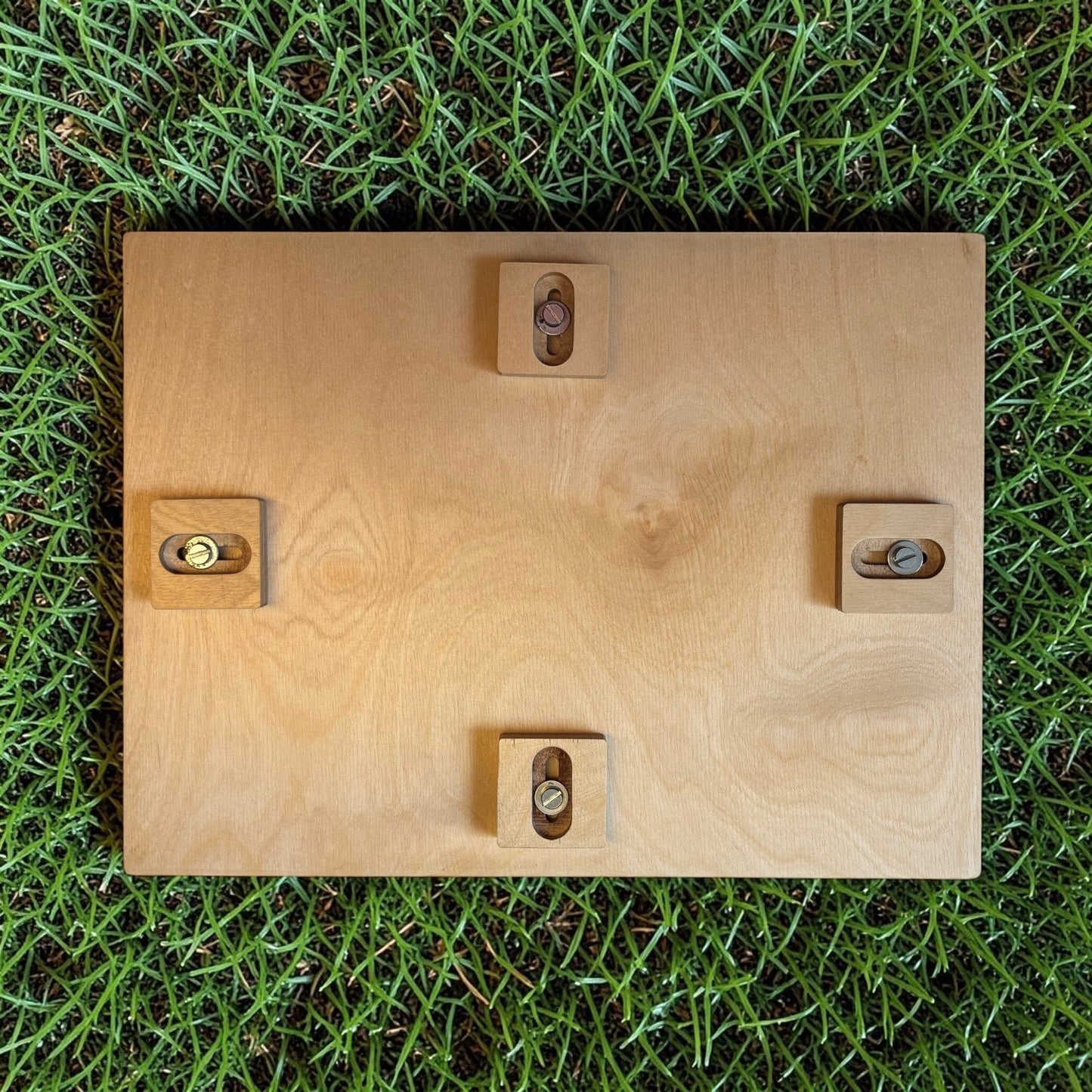 Nomafu wooden crate seat attachment with adjustable metal fasteners, viewed from below on green grass.